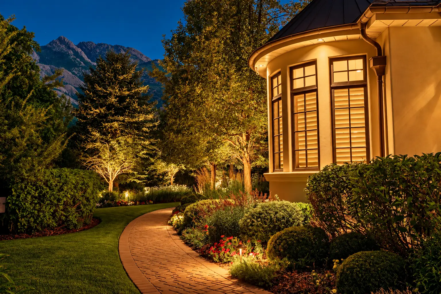 A lit two-story home at dusk surrounded by landscaping