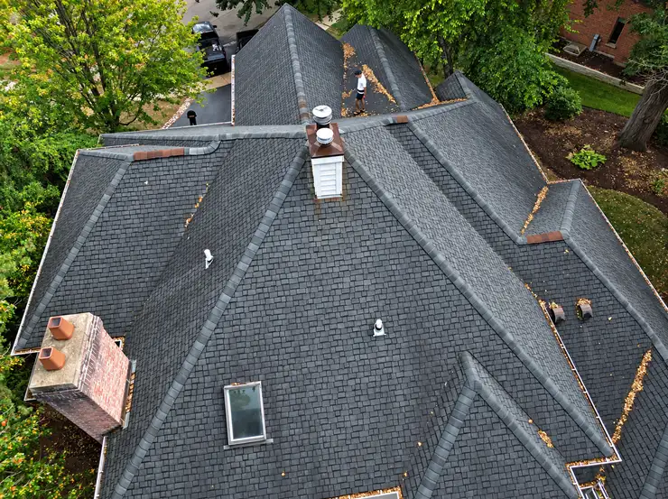 Aerial view of a steep shingled roof with an inspector working on it